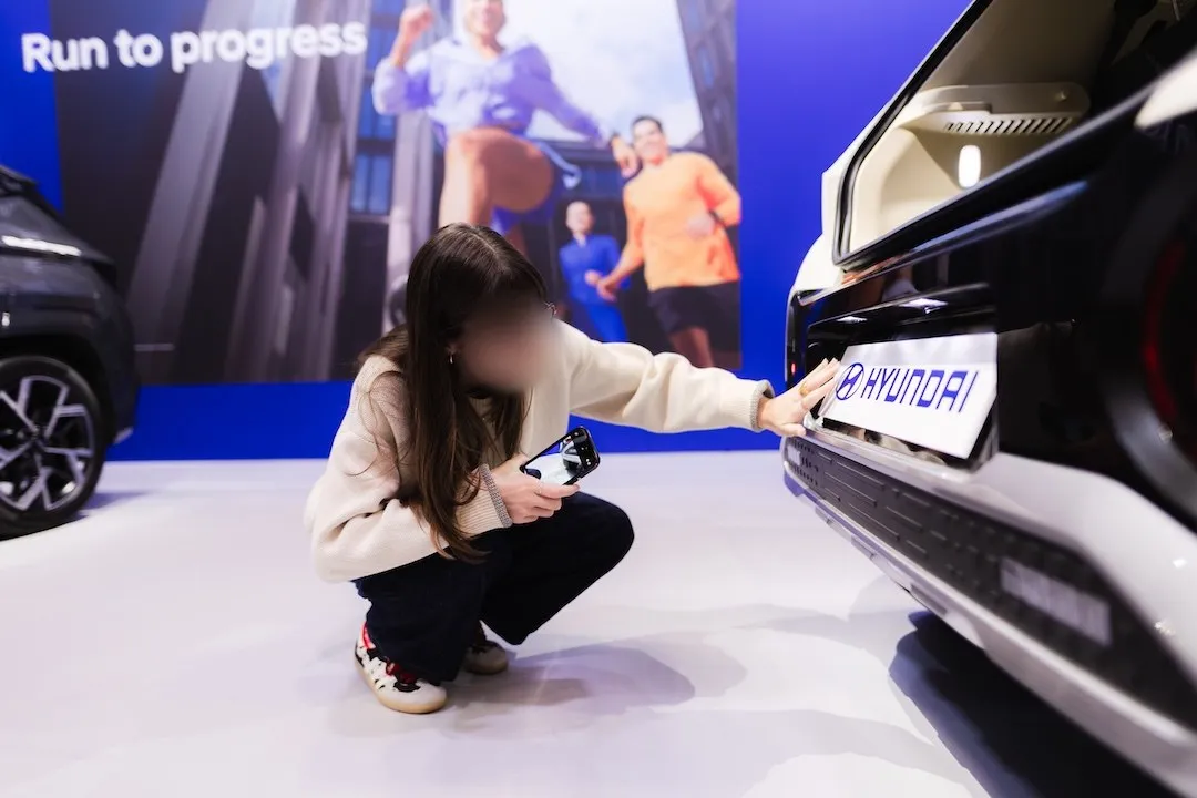 Une visiteuse scanne un QR code caché à l'arrière de la Hyundai Inster, sur un stand aux couleurs de Run to Progress