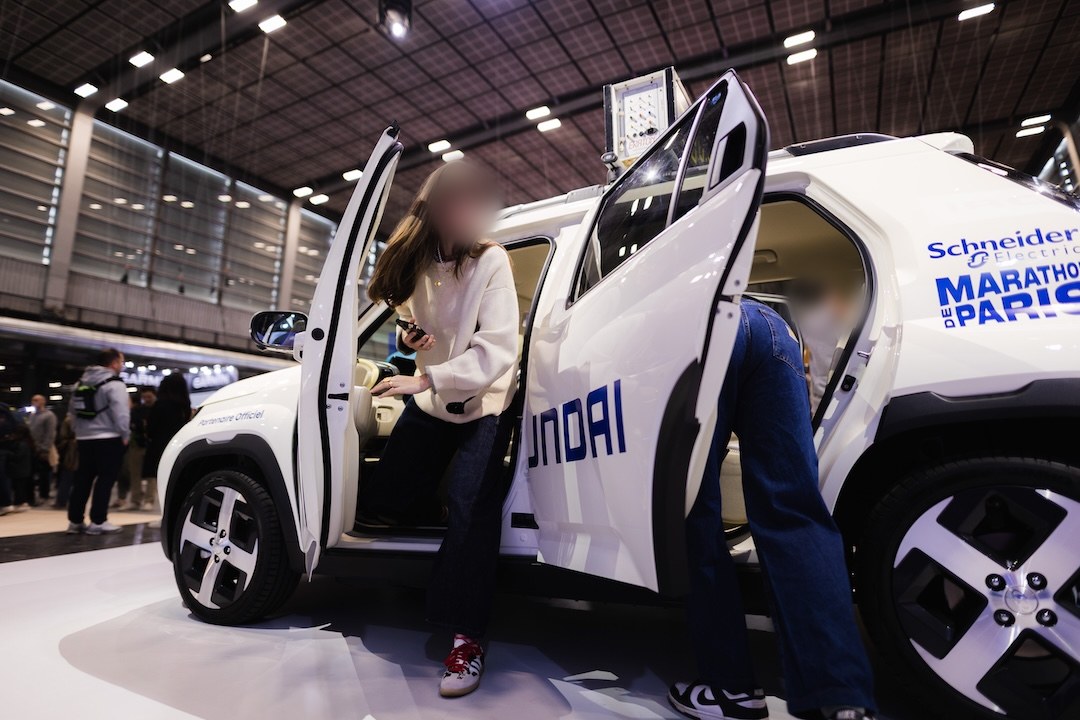 Une visiteuse installée au poste de conduite de la Hyundai Inster, téléphone à la main